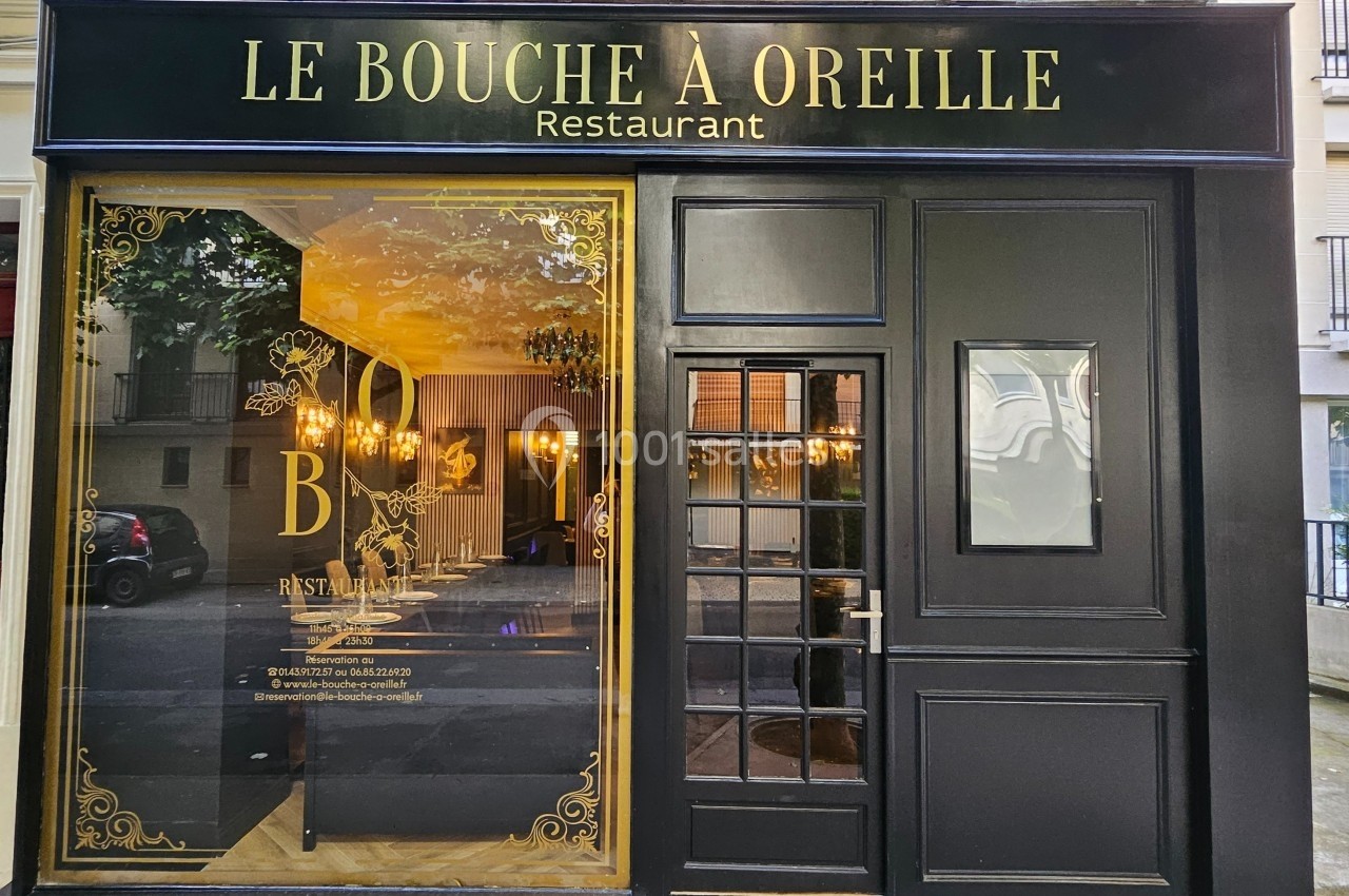 Façade d'un restaurant nommé ’Le Bouche à Oreille’ avec une vitrine dorée et une porte noire vitrée.