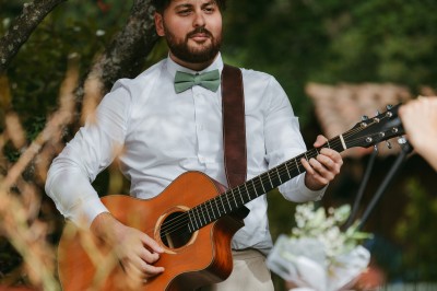 Un homme joue de la guitare acoustique en extérieur, entouré de verdure et de décorations florales.