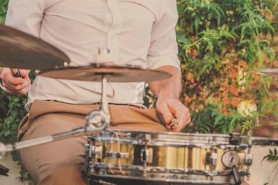 Un musicien joue de la batterie en extérieur, entouré de verdure et éclairé par une lumière douce.