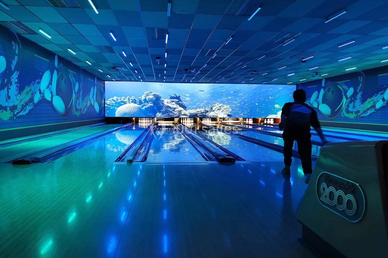 Piste de bowling éclairée par des lumières bleues avec un écran affichant un décor sous-marin en arrière-plan.