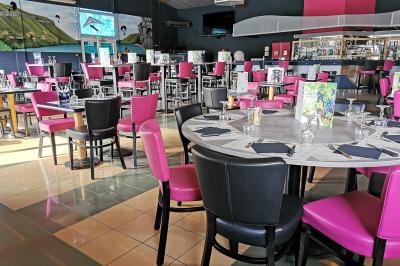 Salle de réception avec une longue table dressée, des chaises rouges et noires, et une fresque murale représentant un…