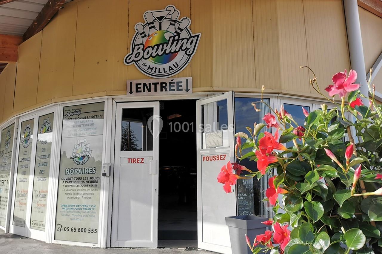 Entrée d'un bowling avec des portes ouvertes, enseigne visible et fleurs rouges au premier plan.