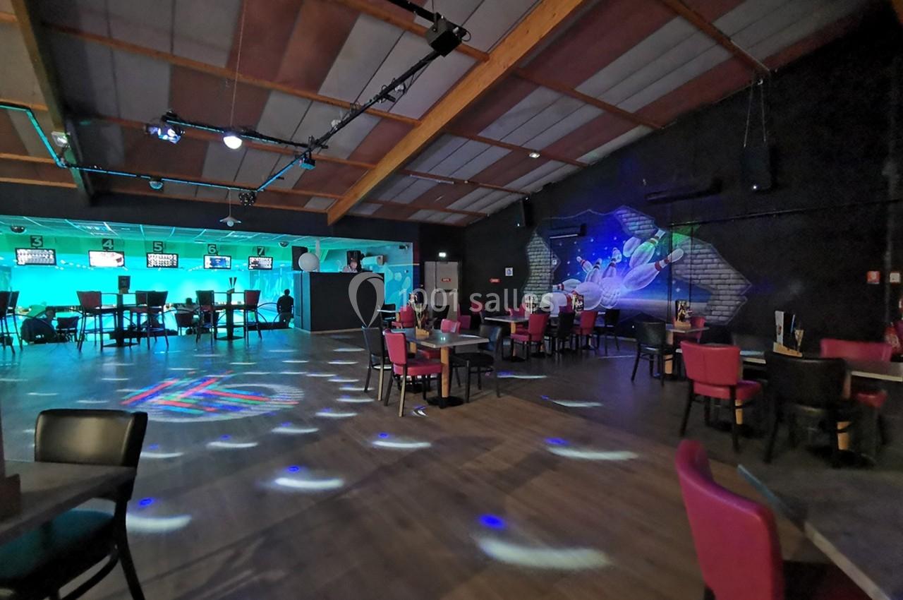 Salle de bowling avec des pistes éclairées, des tables et des chaises disposées dans un espace convivial.