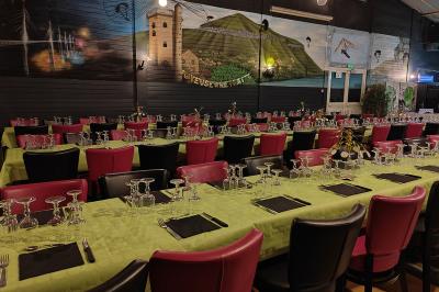 Salle de réception avec une longue table dressée, des chaises rouges et noires, et une fresque murale représentant un…