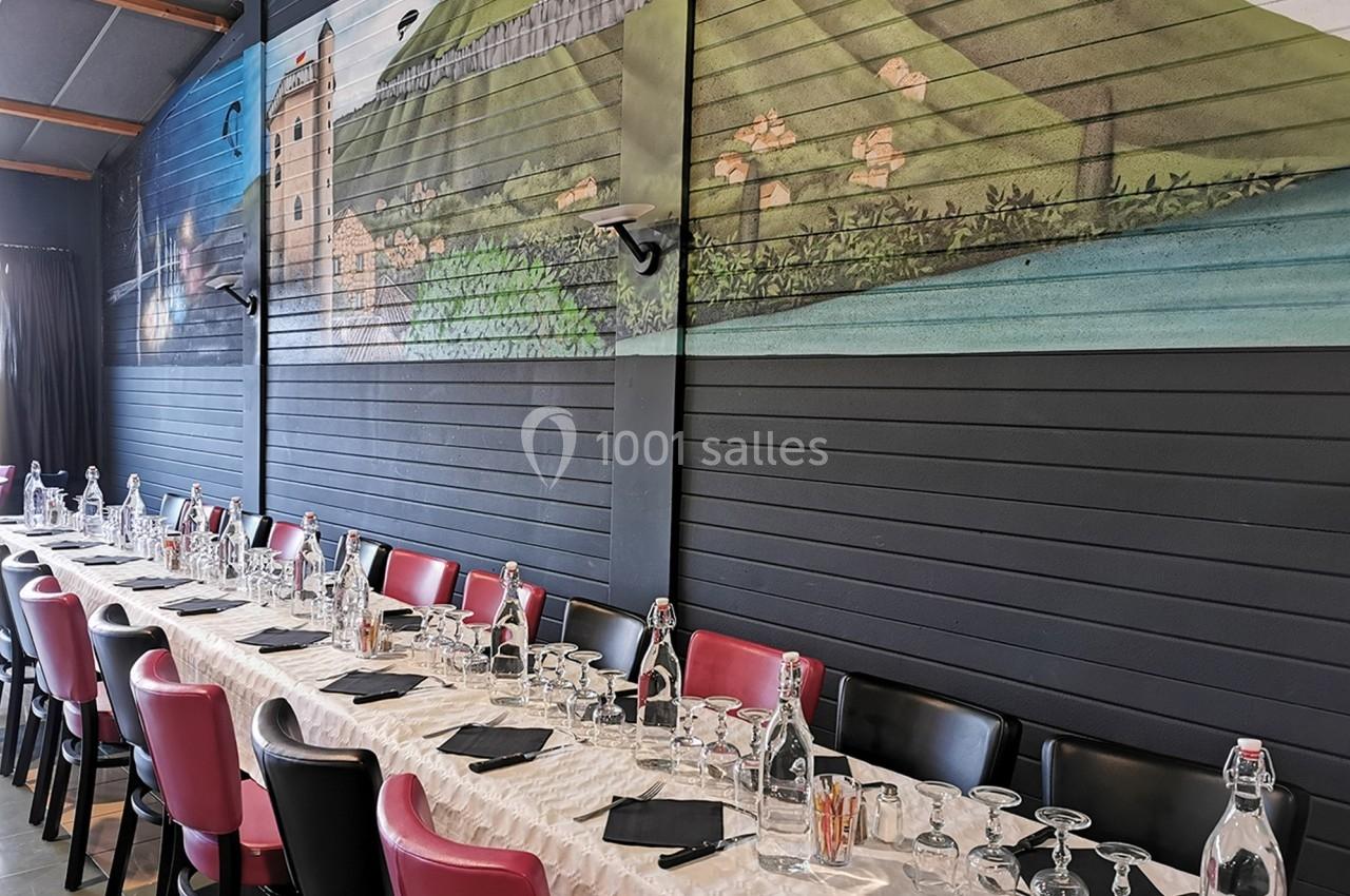 Salle de réception avec une longue table dressée, des chaises rouges et noires, et une fresque murale représentant un…