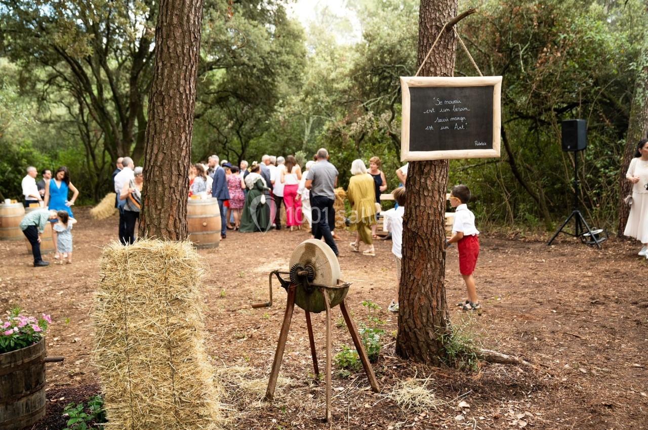 Groupe de personnes réunies dans une clairière boisée, avec une meule ancienne et une ardoise accrochée à un arbre au…