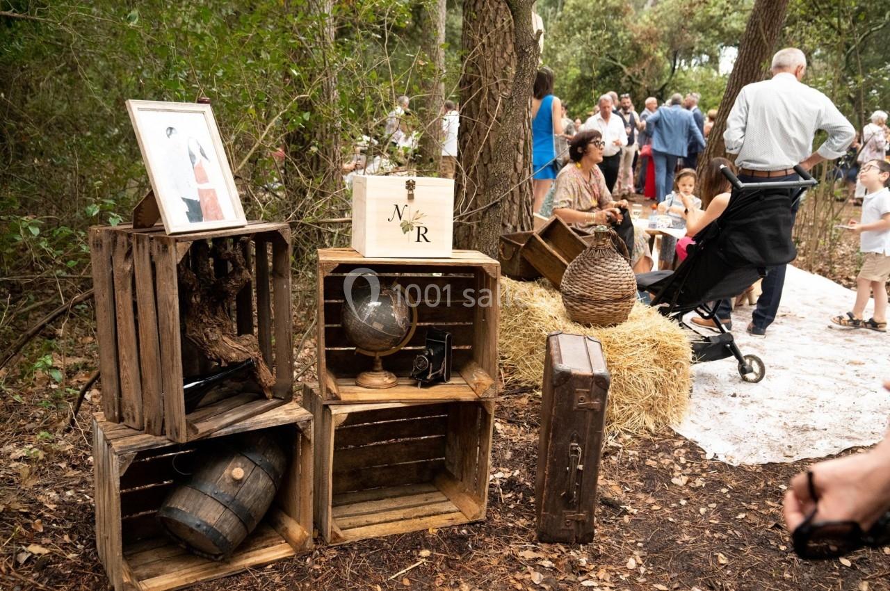 Décoration rustique en bois avec globe, tonnelet et cadres, dans une clairière boisée lors d'un événement en plein air.