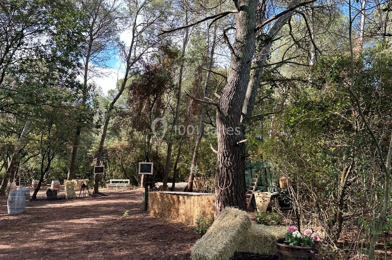Espace extérieur boisé avec des bottes de foin, des barils et des décorations rustiques sous un ciel dégagé.
