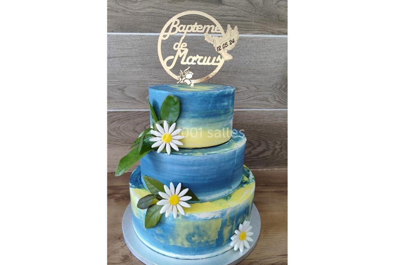 Gâteau de baptême à deux étages, décoré de marguerites et d'un topper en bois avec une colombe et un prénom.