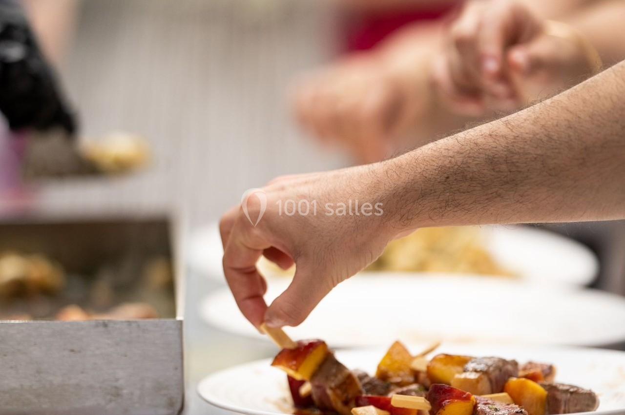 Personne servant des morceaux de viande et de légumes dans une assiette lors d'un buffet en extérieur.