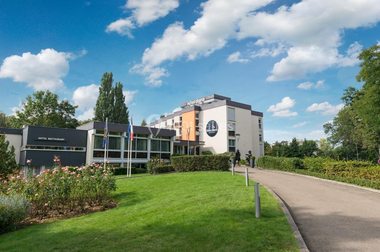 Façade d'un hôtel moderne entouré de verdure, avec un chemin menant à l'entrée principale.