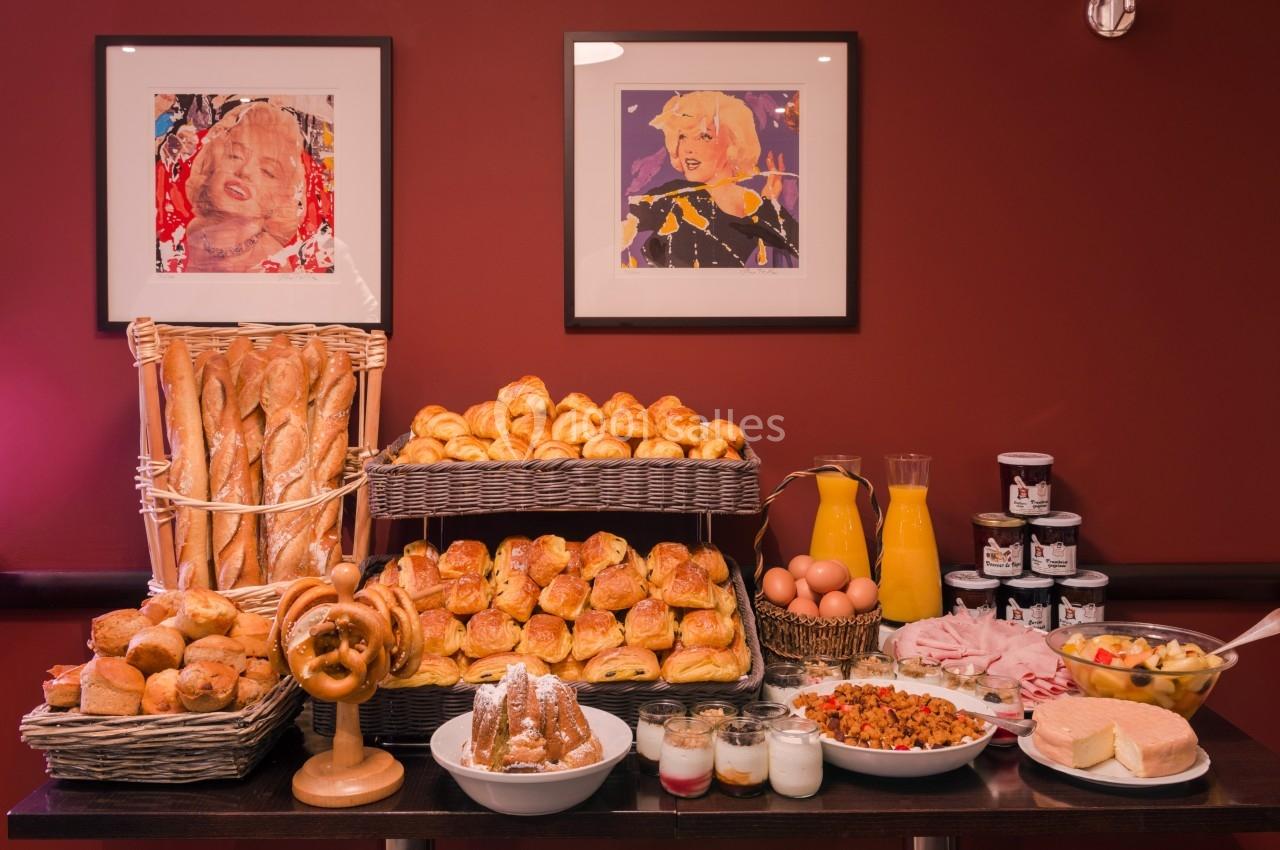 Buffet de petit-déjeuner avec viennoiseries, pains, confitures, jus d'orange, œufs, fruits et yaourts sur une table.