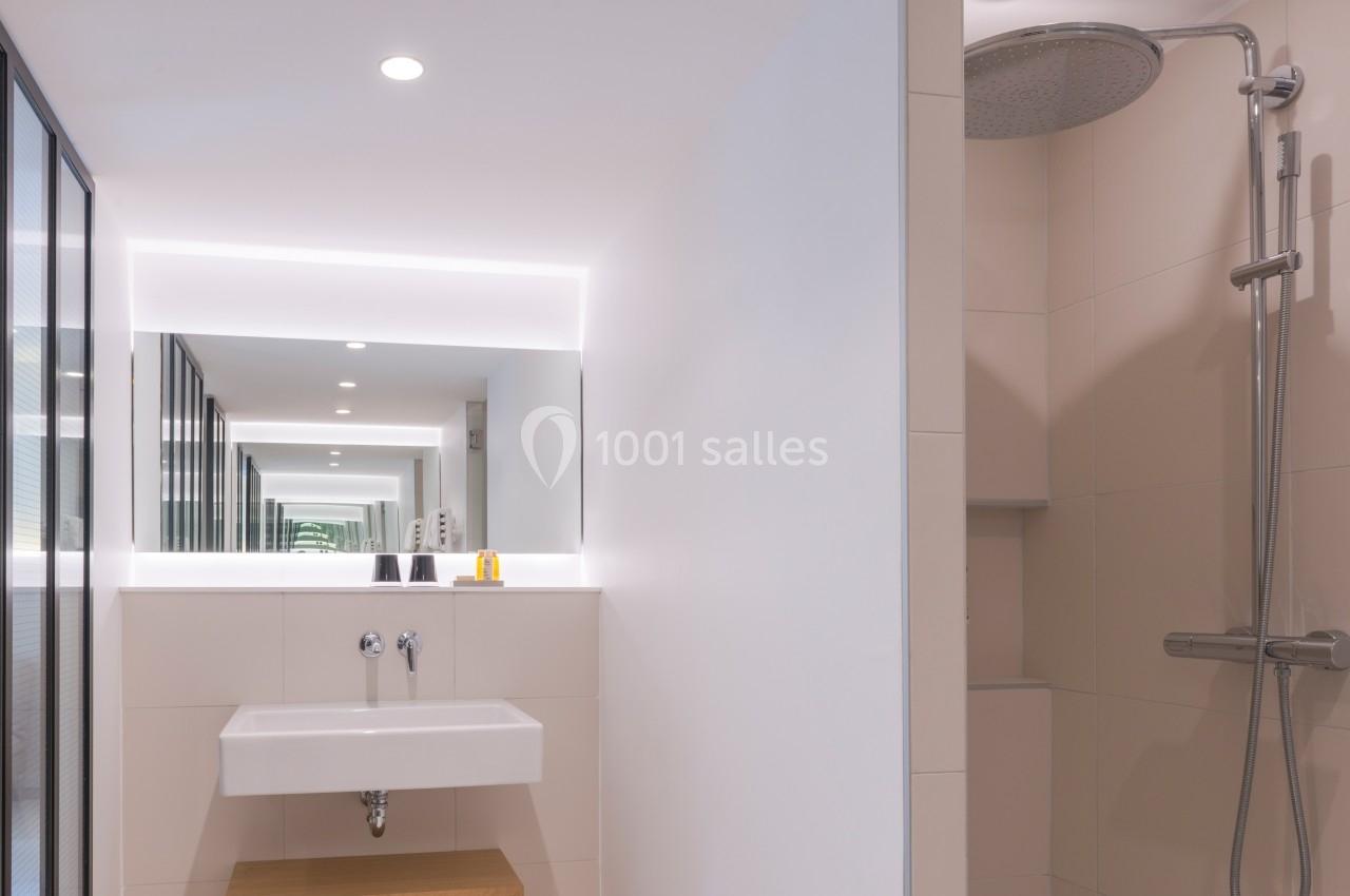 Salle de bain moderne avec lavabo suspendu, grand miroir lumineux et douche à effet pluie.