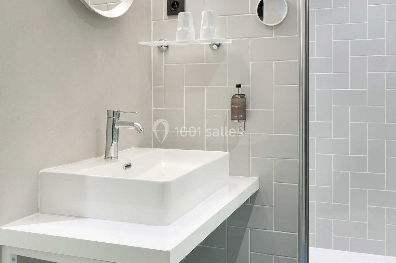 Salle de bain moderne avec lavabo blanc, miroir rond, porte-serviette et douche à paroi vitrée.