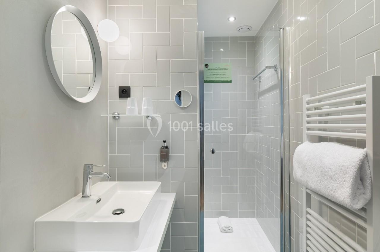 Salle de bain moderne avec lavabo, miroir rond, douche vitrée et porte-serviettes mural avec serviette blanche.