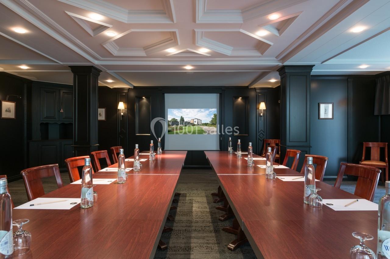 Salle de réunion avec une grande table en bois, chaises alignées, bouteilles d'eau, blocs-notes et écran de projection.