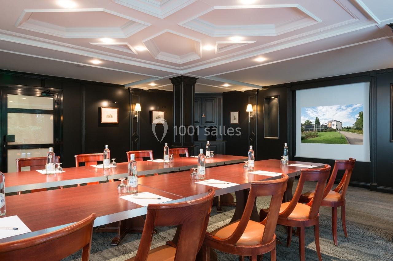 Salle de réunion avec table en bois, chaises, bouteilles d'eau, blocs-notes et écran projetant une image de paysage.