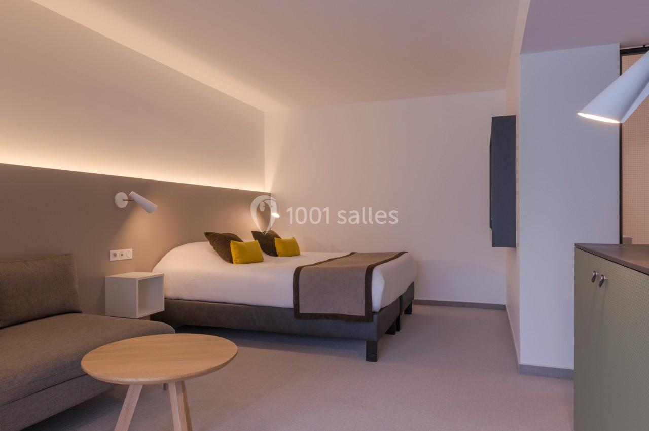 Chambre moderne avec un lit double, un canapé, une table basse en bois et un éclairage tamisé.