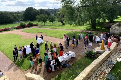 Vue sur un jardin avec pelouse, allées en gravier, parterre de fleurs rouges et bâtiments en pierre sous un ciel dégagé.