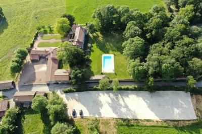 Vue sur un jardin avec pelouse, allées en gravier, parterre de fleurs rouges et bâtiments en pierre sous un ciel dégagé.