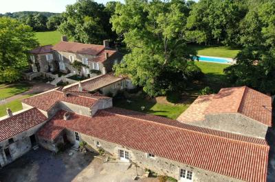 Vue sur un jardin avec pelouse, allées en gravier, parterre de fleurs rouges et bâtiments en pierre sous un ciel dégagé.