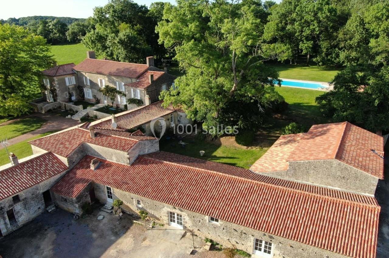 Vue aérienne d'un domaine rural avec bâtiments en pierre, toits en tuiles rouges, piscine et espaces verts environnants.