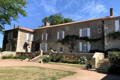 Vue sur un jardin avec pelouse, allées en gravier, parterre de fleurs rouges et bâtiments en pierre sous un ciel dégagé.
