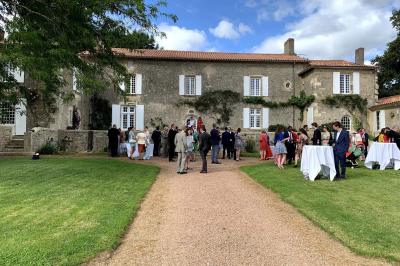 Vue sur un jardin avec pelouse, allées en gravier, parterre de fleurs rouges et bâtiments en pierre sous un ciel dégagé.