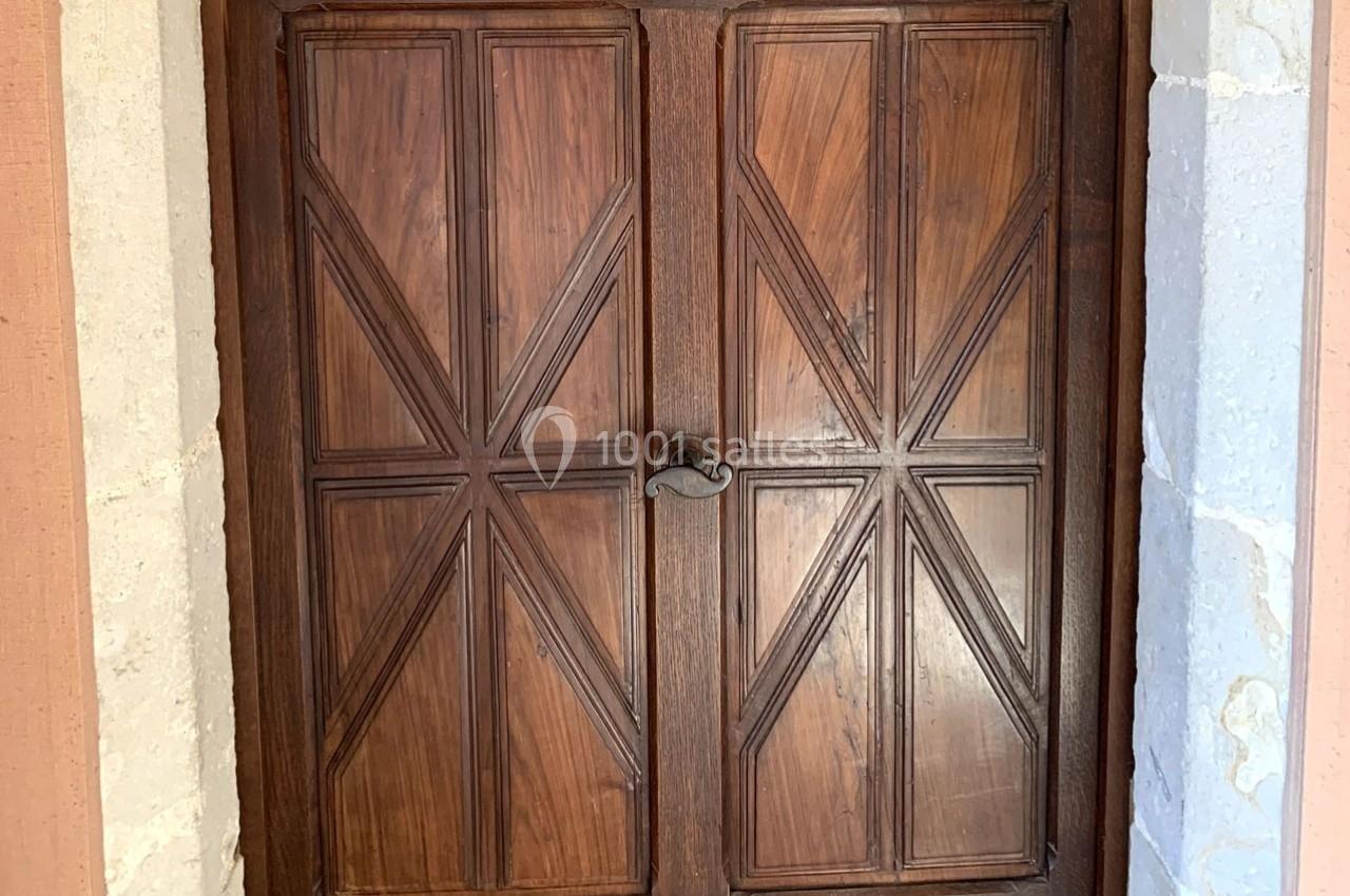 Porte en bois à double battant avec motifs géométriques, encadrée par des pierres claires.