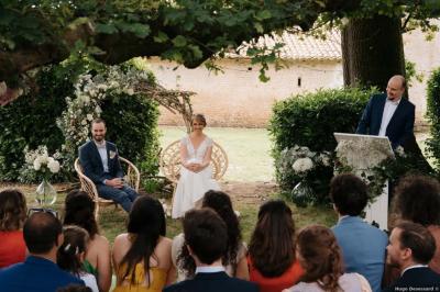 Vue sur un jardin avec pelouse, allées en gravier, parterre de fleurs rouges et bâtiments en pierre sous un ciel dégagé.