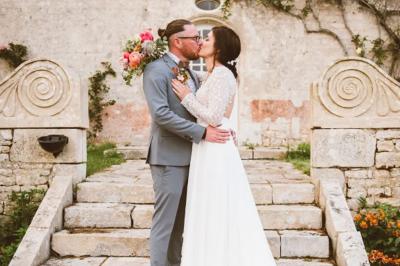 Vue sur un jardin avec pelouse, allées en gravier, parterre de fleurs rouges et bâtiments en pierre sous un ciel dégagé.