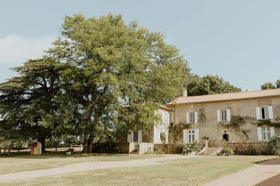 Vue sur un jardin avec pelouse, allées en gravier, parterre de fleurs rouges et bâtiments en pierre sous un ciel dégagé.