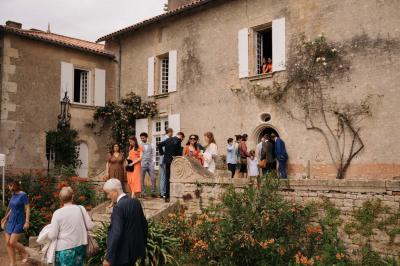 Vue sur un jardin avec pelouse, allées en gravier, parterre de fleurs rouges et bâtiments en pierre sous un ciel dégagé.