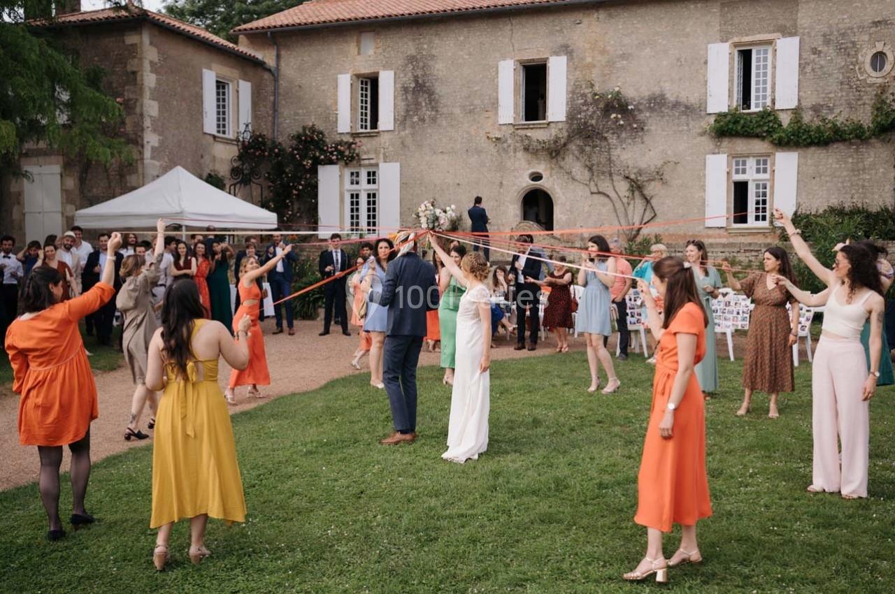 Des personnes participent à une danse traditionnelle avec des rubans colorés dans le jardin d'une maison en pierre.