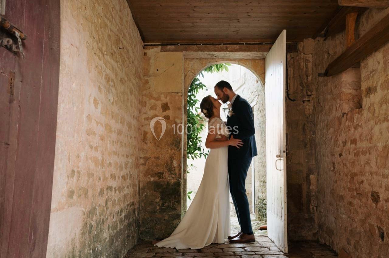 Un couple habillé élégamment s'embrasse dans une entrée en pierre éclairée par la lumière naturelle.