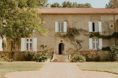 Vue sur un jardin avec pelouse, allées en gravier, parterre de fleurs rouges et bâtiments en pierre sous un ciel dégagé.