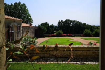 Vue sur un jardin avec pelouse, allées en gravier, parterre de fleurs rouges et bâtiments en pierre sous un ciel dégagé.