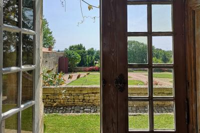 Vue sur un jardin avec pelouse, allées en gravier, parterre de fleurs rouges et bâtiments en pierre sous un ciel dégagé.