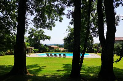 Vue sur un jardin avec pelouse, allées en gravier, parterre de fleurs rouges et bâtiments en pierre sous un ciel dégagé.