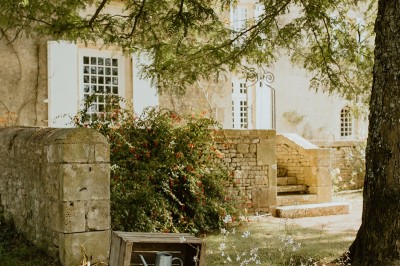 Miniature Location salle L'Orbrie (Vendée) - Le Logis des Arçonnières #70 Un couple marche dans un jardin verdoyant en direction d'une grande maison en pierre avec des volets blancs.