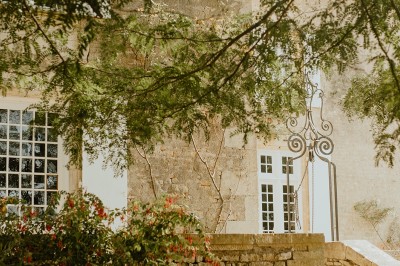 Miniature Location salle L'Orbrie (Vendée) - Le Logis des Arçonnières #71 Un couple marche dans un jardin verdoyant en direction d'une grande maison en pierre avec des volets blancs.