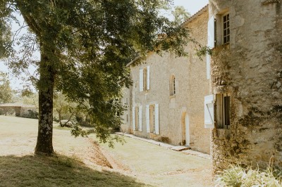 Miniature Location salle L'Orbrie (Vendée) - Le Logis des Arçonnières #72 Un couple marche dans un jardin verdoyant en direction d'une grande maison en pierre avec des volets blancs.