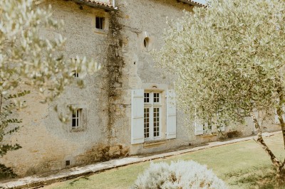 Miniature Location salle L'Orbrie (Vendée) - Le Logis des Arçonnières #73 Un couple marche dans un jardin verdoyant en direction d'une grande maison en pierre avec des volets blancs.