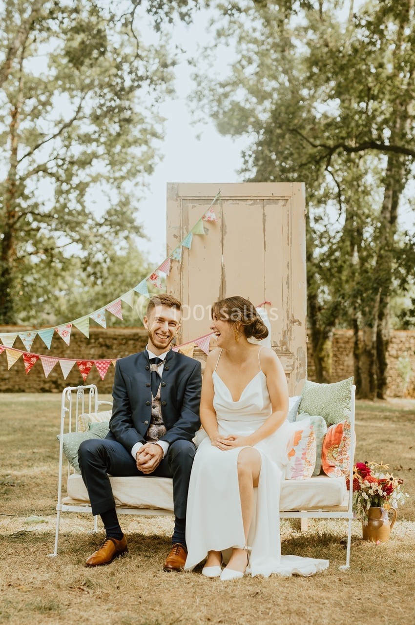 Un couple assis sur un banc dans un jardin décoré de fanions colorés et d'une porte vintage en arrière-plan.
