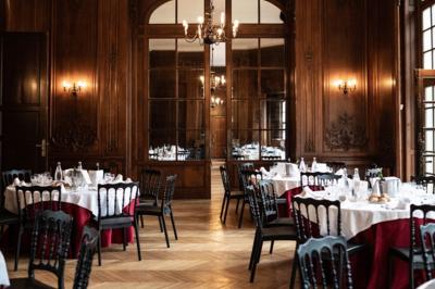 Salle élégante avec tables rondes dressées pour un repas, décorée de rideaux dorés, miroirs et mobilier classique.