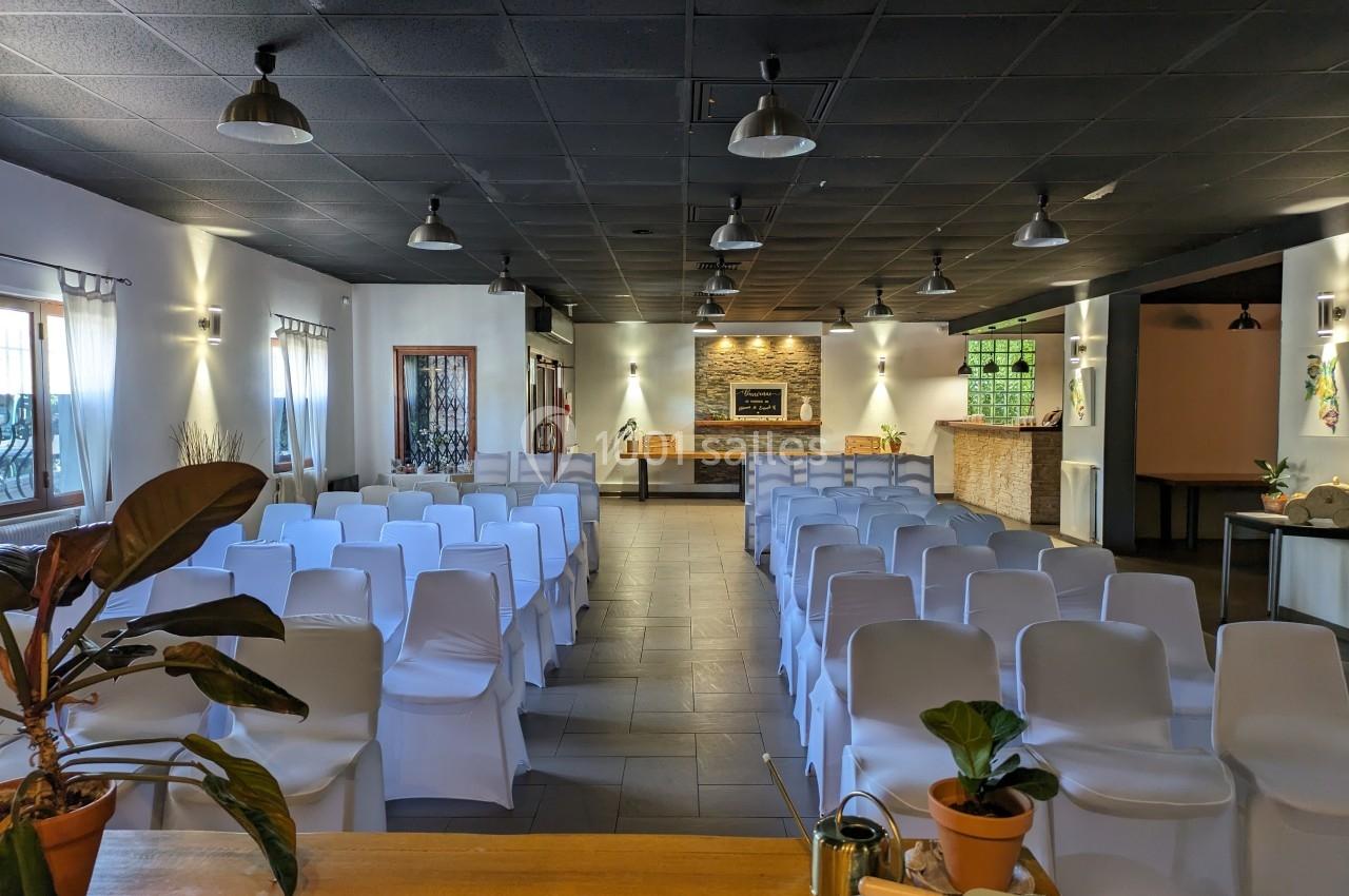 Salle de réunion avec des chaises blanches alignées, éclairage tamisé et décorations végétales sur un comptoir en arrière…