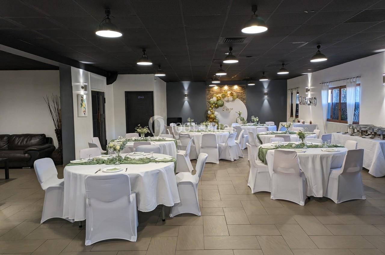 Salle de réception décorée avec des tables rondes nappées de blanc, ornées de centres de table floraux.