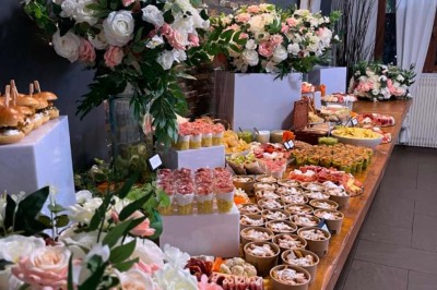 Buffet varié avec fleurs décoratives, comprenant amuse-bouches, desserts et boissons, présenté sur une longue table.