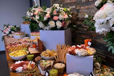 Buffet varié avec fleurs décoratives, comprenant amuse-bouches, desserts et boissons, présenté sur une longue table.