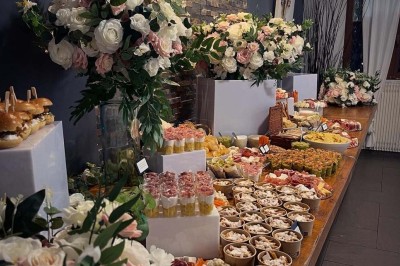 Buffet varié avec fleurs décoratives, comprenant amuse-bouches, desserts et boissons, présenté sur une longue table.